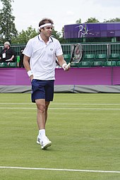 Photo d'un joueur de tennis gaucher qui est en train de demander une balle à un ramasseur situé hors champ