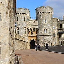 A photograph of a stone gatehouse, with two large, circular towers on each side of the gateway dominating the picture. A stone wall stretches alongside the left hand side of the picture.