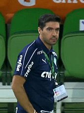 Um homem de meia-idade, barba levemente feita, vestindo uma camisa azul-escura. Ele está olhando para a direita, com semblante de concentrado.