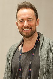 A close-up picture of a smiling man wearing a lanyard around his neck.