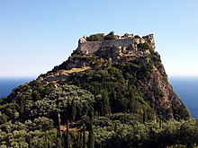 château au sommet d'un piton rocheux arboré.