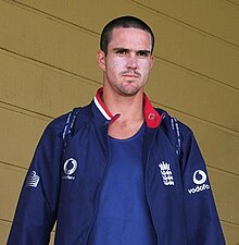 A man with a shaven head in a blue top and shirt.