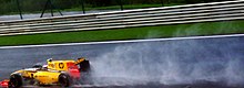 A black, yellow and red Formula One car racing at speed on a wet track