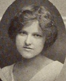 A young white woman with sandy hair dressed to the nape, wearing a white top