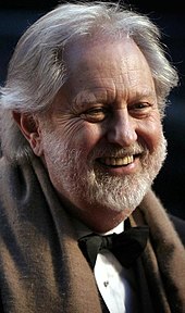 A profile image of David Puttnam. An older Caucasian male with shoulder-length white hair and a short white beard. The man is shown from his front-right profile, facing right and smiling away from the camera.