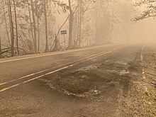 A smoky scene on a rural two-lane highway with ash and debris on the road surface