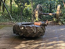 A large tyre on chains in a courtyard - a child's feet and legs poke out of the middle wearing gumboots. The evening sun is dappled.