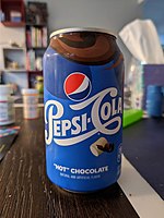 This is an image of the front of a Pepsi "Hot" Chocolate Flavor can. The top of the can is emblazoned with the Pepsi logo in its older classic font reading "Pepsi Cola". Above that is the standard Red White and Blue Pepsi Logo. Beneath and slightly to the right of the font is a marshmallow and a sliver of chocolate. Closer to the bottom there contains the text "'Hot' Chocolate". Under that is the text "Natural and Artificial Flavor" The bottom right of the whole front of the can contains the standard callorie label stating that the can has "150 calories per can" with the text describing the cans volume of liquid below stating "12 Fluid Ounces (355 millileters)". The whole can is surrounded by liquid chocolate swirls flowing from top to bottom and left to right.