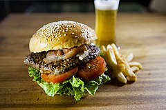 A brown meat patty between slices of yellow American cheese, topped with sliced pickles and lettuce, sandwiched in a sesame seed bun