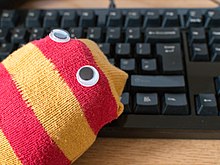 A sock puppet with eyes in front of a computer keyboard