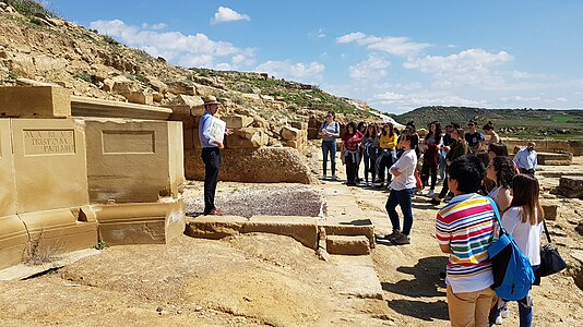 Javier Andreu explicando y mostrando a los visitantes del yacimiento romano de Los Bañales (Uncastillo) el contenido de los restos hallados (2018).