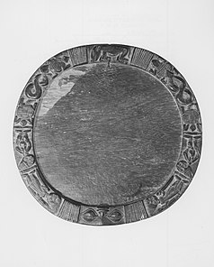 A roughly circular wooden tray with a raised border carved with human and animal figures.