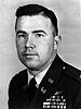 Head and shoulders of a dark-haired white man wearing a dark military jacket with four rows of ribbon bars and a winged pin on the left breast.