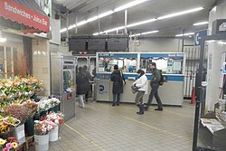 View of the fare control area at ground level. There is a station agent booth in the background and a florist to the left.