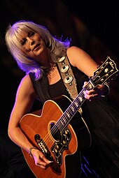 A Caucasian woman with white hair playing a guitar
