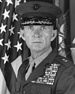 A black and white headshot of Livingston wearing his military dress uniform with a hat and ribbons. He is looking directly at the camera and there is an American flag in the background.