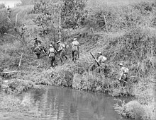 Soldiers slowly advance up a hill along the side of a waterway