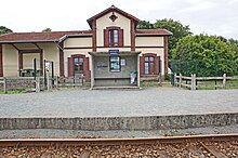 L'abri de quai de la halte avec les informations affichées. En arrière-plan, l'ancienne gare