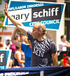 A young man waves at a parade, while a campaign sign with his name, Gary Schiff, is held up behind him.