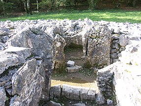 Internal view of cairn. A rectangular transept chamber is shown, with limestone orthostats and the remains of a sill at its entrance from a passageway. Boulders are piled up to its left, right and rear. The image has been taken from the chamber's pair, on the other side of the passageway.