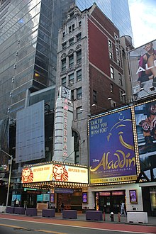 View of the facade in 2021, as seen from across 42nd Street. There is an electronic marquee just above the entrance, advertising the Lion King. An electric sign with a clock and the words "New Amsterdam" is located above the marquee.