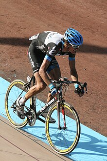 A road racing cyclist wearing a black and white jersey with blue trim and a conspicuous accented e on the shoulder, a blue helmet, and sunglasses.