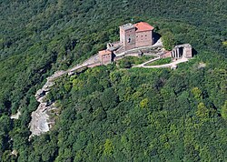 Photo of Trifels Castle as see from Martinstrum. The Castle's square brick towers sit on top of the rocky peak of a hill in a forested valley.