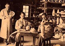 Black and white photograph of the interior of a workshop with three people at work.