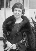 Black and white image of Milagros Benet de Mewton wearing a fur coat while standing on a sidewalk.
