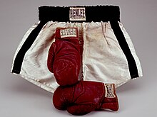 Deux gants de boxe rouges devant un short de boxe noir et blanc.