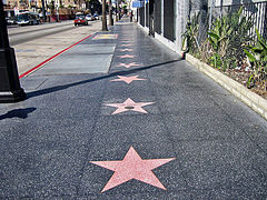 Several stars on the Walk of Fame at 6801 Hollywood Boulevard, with اجرای خیابانی and passersby