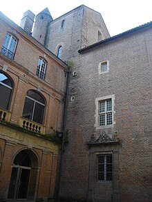 Photo couleur montrant une tour dépassant d'une toiture à l'angle de deux ailes d'un château en briques rouges.