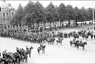 Parad på Gustaf V:s födelsedag 1928. Förbimarsch för platschefen överste Pontus Reuterswärd på skolplan framför Eric Ugglas skola. I bakgrunden militärsstabens byggnad i Skövde.