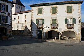 Vue d’une maison de deux étages, aux volet verts fermés, avec deux arches rez-de-chaussée.