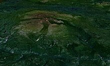 Vegetated terrain with a rocky, gently sloping mountain with large valleys carved into its slopes rising over the landscape.