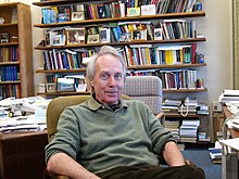 Colour photograph of Antony Jameson in pullover, relaxed, seated in a study with many books and papers