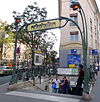 Photographie d'une bouche de métro d'où sortent, au premier plan deux hommes portant des chemises à manches courtes, un troisième se tenant debout sur les premières marche et téléphonant.