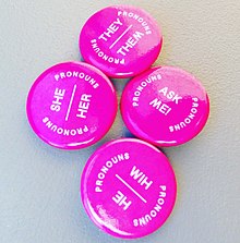Four pin-on metal badges with labels "He Him", "She Her", "They Them", and "Ask Me!"
