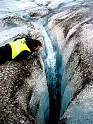 A crevasse created by water drilling a hole tens of meters deep into the glacier ice. Our skidoo guide inspects the crack. Langjökull glacier. July 2006.