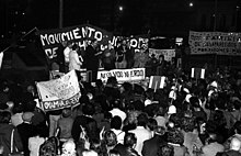 A crowd of people looking at five people standing on a platform in front of a banner that says "Movimento Judío por los Derechos Humanos"