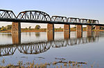 Four truss sections of a railway bridge, supported by stone pillars.