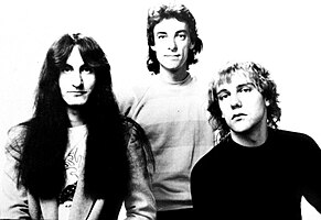 Rush promotional image with Lee, Peart, and Lifeson, standing left to right in black and white