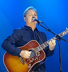 Country music singer Steve Wariner, singing into a microphone and playing an acoustic guitar