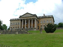 Beau manoir en haut d'une pente gazonnée, avec grand porche à colonnes et fronton, vu en contre-plongée