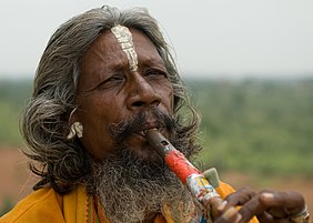A man playing flute in Orchha, with a white tilak on his forehead, and holy saffron-coloured clothes.