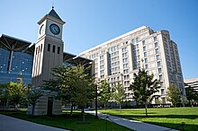 Two modern glass and concrete building side by side in front of an open grass lawn which has a short clocktower on the left side.