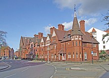 A terrace of red-brick houses with tiled roofs and an octagonal turret at each end. Each of the houses is different, and include bay windows, different sized gables and dormers.