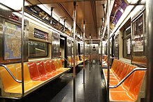 The interior of an R62A car on the 1 train. Its seats are yellow, red, and orange, and it has several advertisements hanging above.