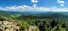 Vue d'un sommet rocheux sur des collines boisées.