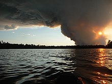 The sun sets over a wilderness lake behind the smoke from a large wildfire.